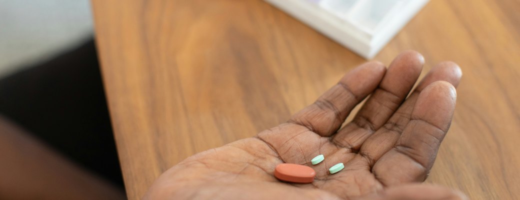 A hand holding tablets on a wooden table, beside a pill organiser