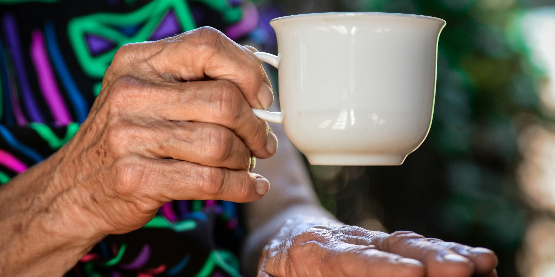 Les mains d’une personne âgée tenant une tasse blanche