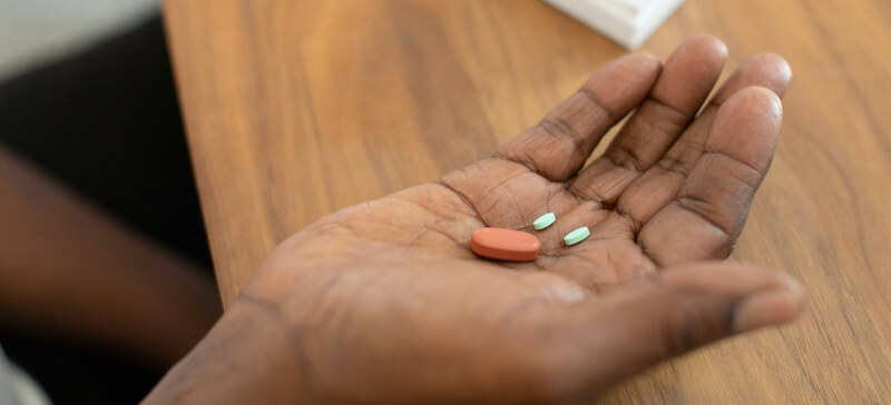 A hand holding tablets beside a pill organiser at home