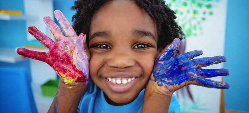 A smiling child holding up hands covered in red and blue paint