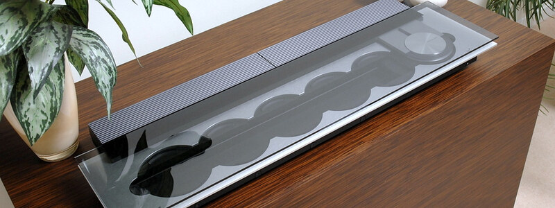 A Bang & Olufsen CD player on a walnut sideboard, its discs visible behind glass, with a plant beside it